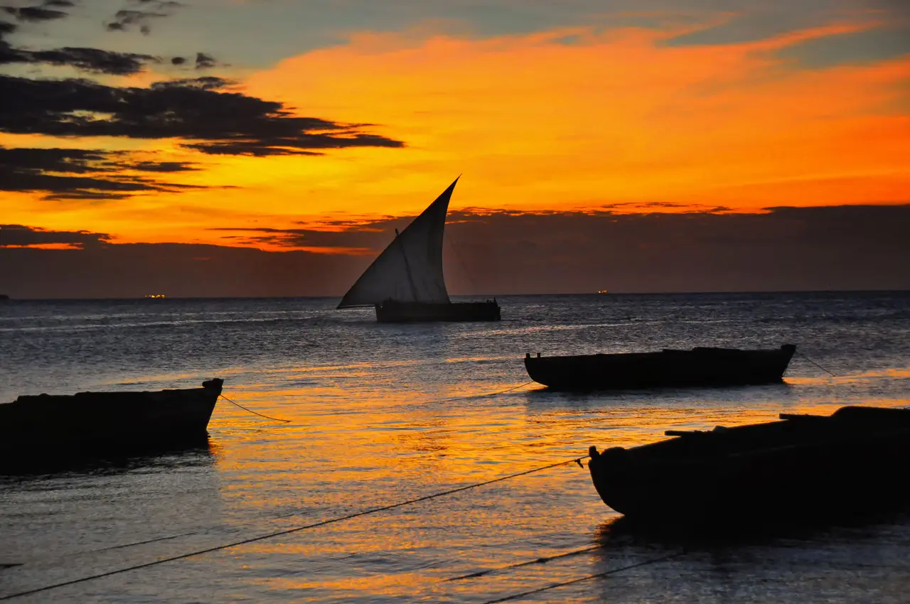 Un dhow con la vela spiegata al tramonto davanti a Zanzibar
