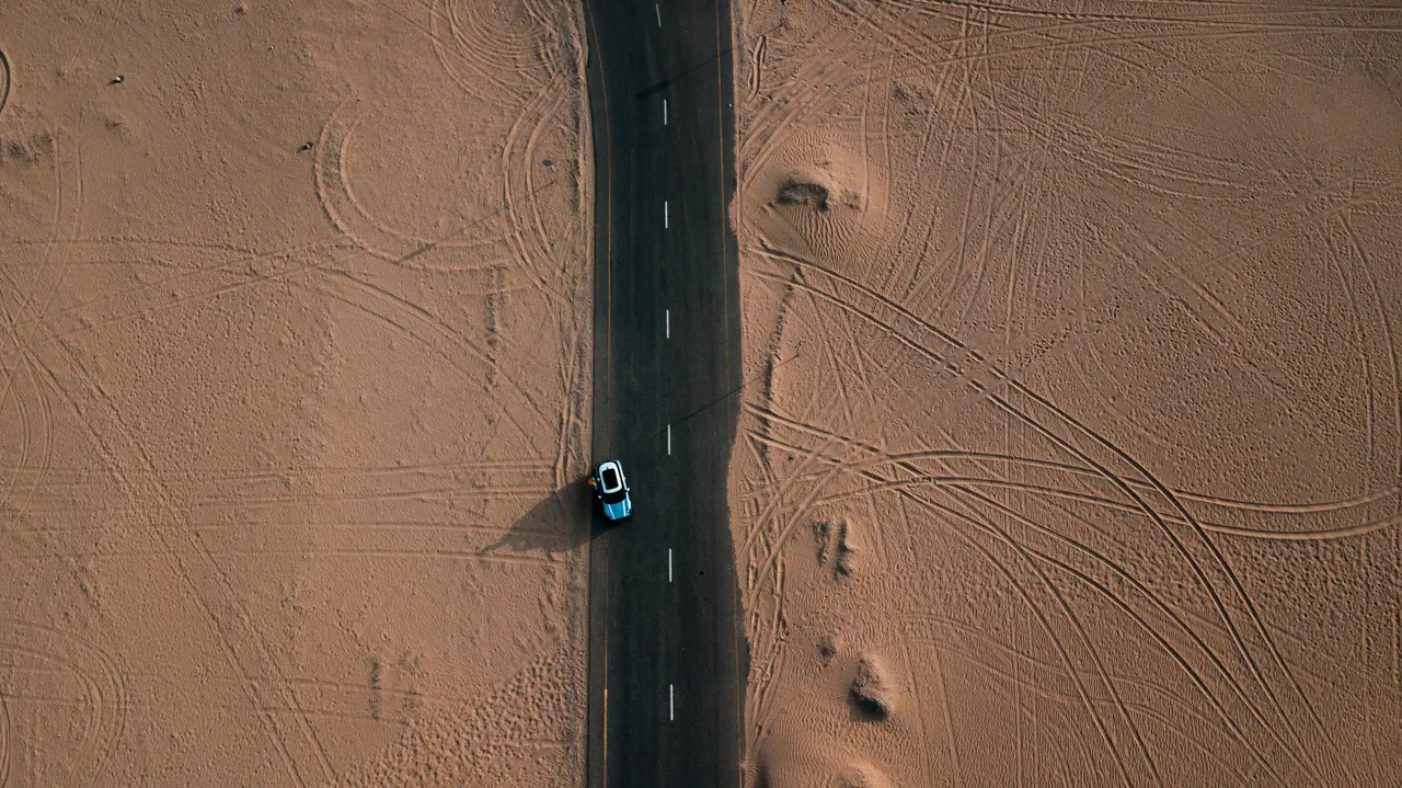 Auto su una strada asfaltata che attraversa il deserto, vista dall’alto